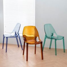 three different colored chairs sitting on top of a hard wood floor next to a window