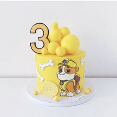 a birthday cake with yellow frosting and dog figures on the top, sitting on a white table