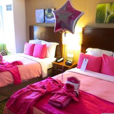 two beds in a hotel room with pink sheets and pillows on them, one has a star shaped balloon that says happy birthday