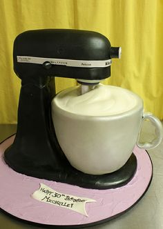 a black and white mixer sitting on top of a pink plate with a yellow curtain behind it