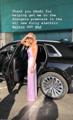 a woman in a pink dress standing next to a black car with its doors open