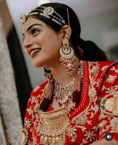 a woman in a red and gold bridal outfit smiles at the camera while wearing jewelry