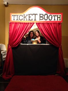 two women standing in front of a red curtain with the words ticket booth on it