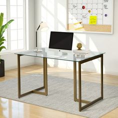 a glass desk with a computer on it in front of a large poster and potted plant