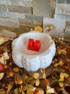 two red candles sitting in a white bowl on top of leaves and acorns