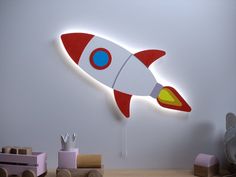 a red and white rocket ship shaped wall light on the side of a wall next to toys