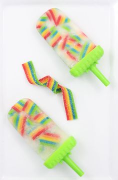 two popsicles with rainbow colored candy on them sitting on a white plate next to each other