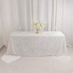 a table with white flowers and napkins on it in front of a curtained window