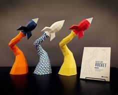 three origami rockets sitting on top of a table next to an open book