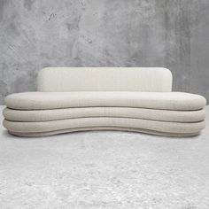 an upholstered sofa with four pillows on it's back and sides, against a concrete wall