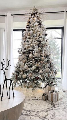 a white christmas tree in a living room decorated with silver and gold ornaments on it's branches