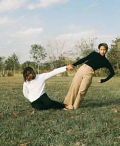 two people in a field holding hands with one person on the ground and another standing behind them