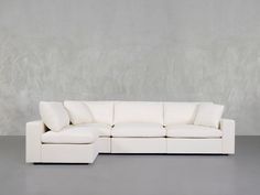 a white sectional sofa with pillows on the top and bottom part, against a gray wall