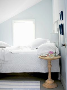 a bed with white sheets and pillows on top of it next to a small table