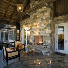 a stone fireplace in the middle of a living room with chairs and tables around it