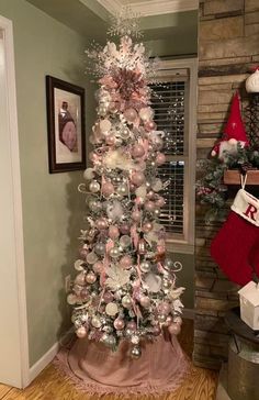 a decorated christmas tree with pink and silver ornaments in a living room next to a fireplace