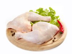 two raw chicken legs on a wooden plate with lettuce and red chili peppers