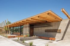 the entrance to a modern building with wooden roof and benches on the outside, in front of a blue sky