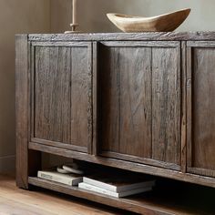 an old wooden cabinet with a bowl on top and some books in the bottom drawer