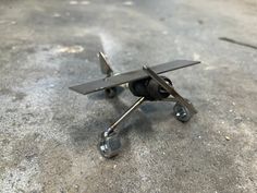 a small metal airplane sitting on top of a cement floor next to a wire spool