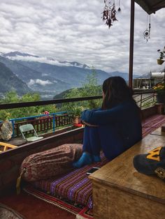 a woman sitting on top of a wooden bench next to a table under a cloudy sky