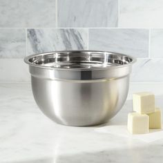 a stainless steel mixing bowl next to cubes of butter on a marble countertop