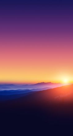 the sun is setting on top of a mountain with fog in the valley behind it