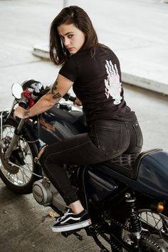 a woman sitting on the back of a motorcycle with her hand on the handlebars