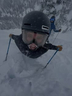 two people are skiing down a snowy mountain side with ski poles in their hands and helmets on