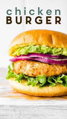 a chicken burger with lettuce, tomato and onion on a white wooden table