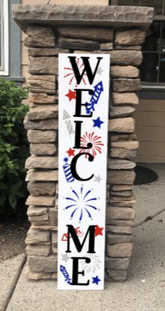 a welcome sign on the side of a stone pillar in front of a building with flags and fireworks