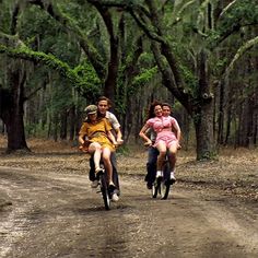 three people riding bikes down a dirt road