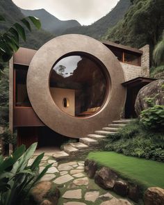 an unusual house in the mountains with a circular window and stone steps leading up to it