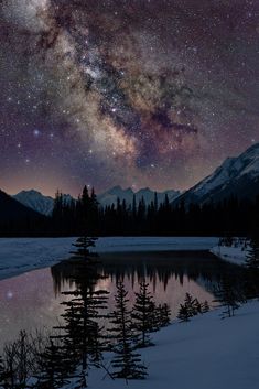 the night sky is filled with stars above a mountain lake and snow - capped mountains