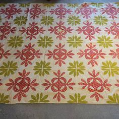 a quilted table runner with red and green flowers on white fabric, sitting on the floor