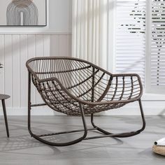 a wicker chair sitting in front of a window next to a table with a vase on it