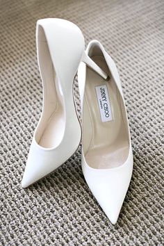 two white high heel shoes sitting on top of a carpet