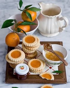 there are some cookies and oranges on the table with honey in bowls next to them