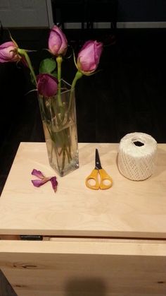 a vase with flowers and scissors on a table next to a spool of twine