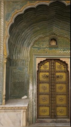 an ornate doorway with gold doors and carvings on the walls is flanked by a marble bench