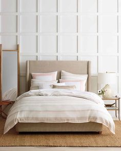 a bed with white and pink pillows in a large room next to a mirror on the wall