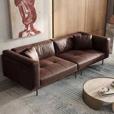 a brown leather couch sitting in a living room next to a painting on the wall