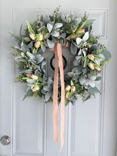 a wreath on the front door with flowers and greenery hanging from it's side