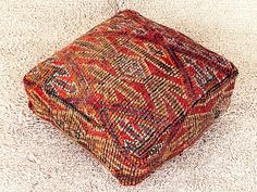 an orange and red ottoman sitting on top of a white carpeted floor next to a wall