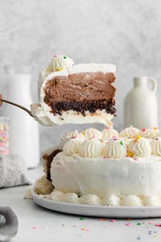 a person holding a fork with a piece of cake on it and the rest of the cake in the background