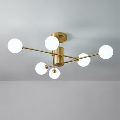 a ceiling light with five white balls hanging from it's center and four gold arms