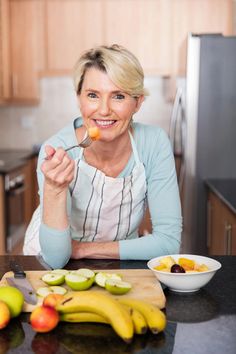 a woman sitting at a kitchen counter eating food from a bowl with fruit in front of her