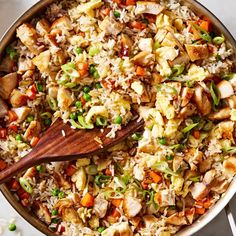 a pan filled with rice and vegetables on top of a white countertop next to a wooden spoon