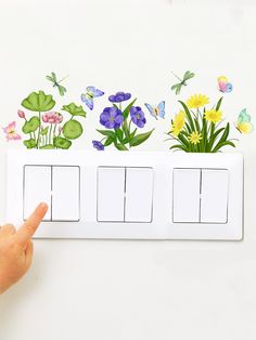 a hand is pointing at a light switch with flowers and butterflies on the wall behind it