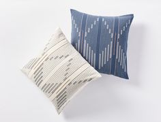 two blue and white pillows sitting next to each other on top of a white surface